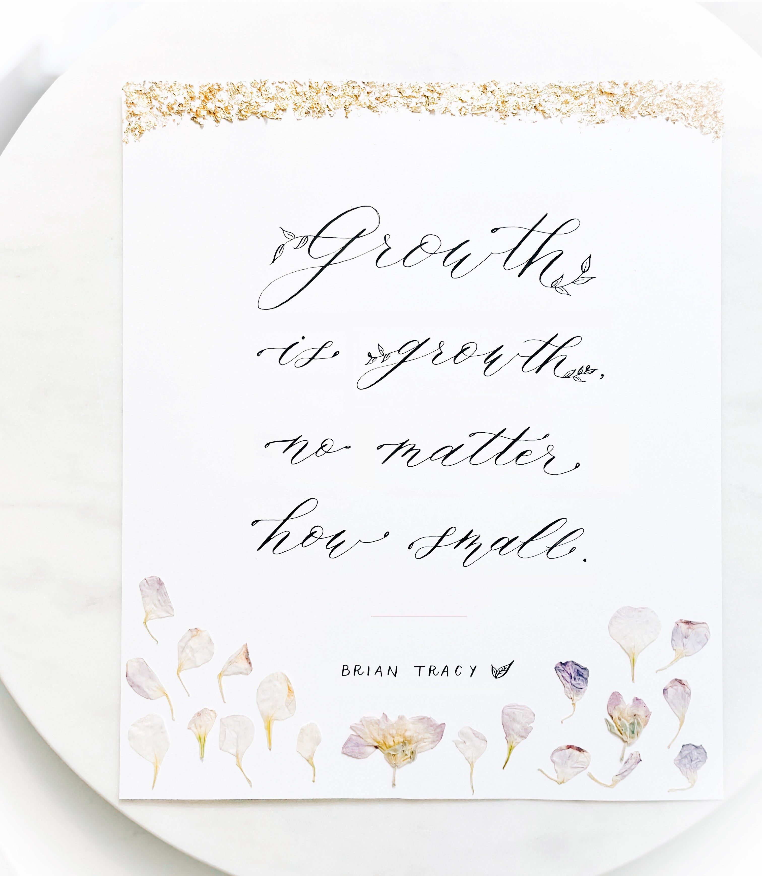 Handwritten modern calligraphy quote art with gold leaf accents and pressed flowers, created using pointed pen lettering.