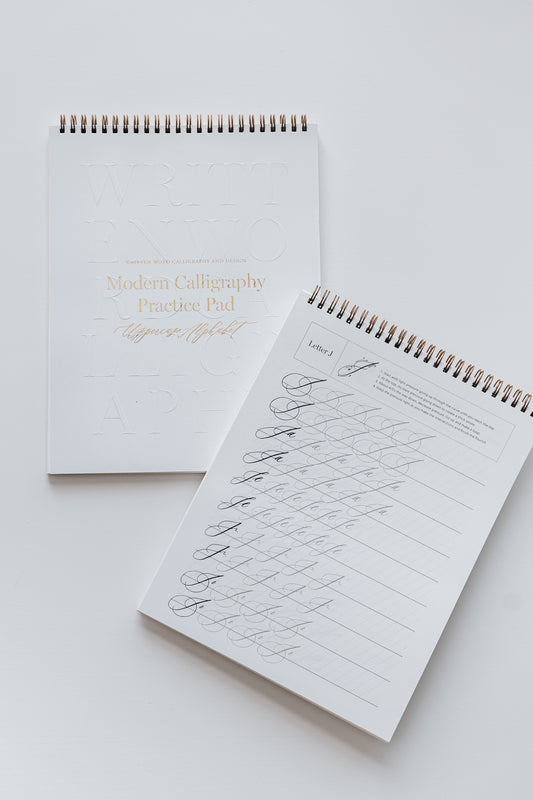 Two modern calligraphy practice pads with letters and examples for beginners, with spiral binding and gold accents