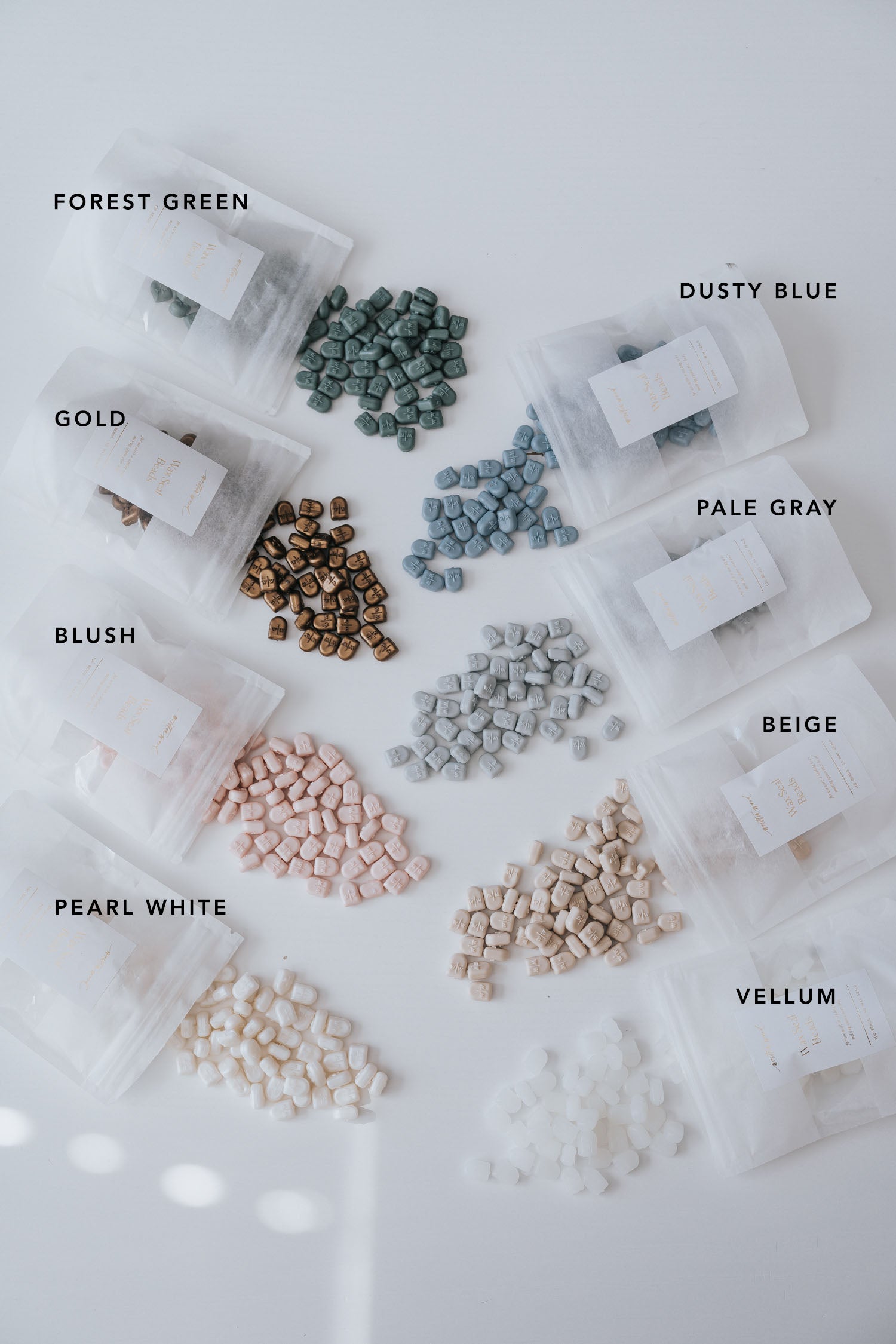 Assorted wax seal beads in eight colors, labeled and spilling from translucent pouches onto a white surface