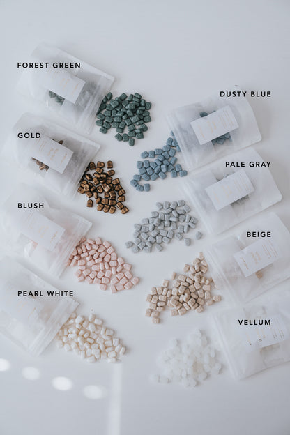 Assorted wax seal beads in eight colors, labeled and spilling from translucent pouches onto a white surface