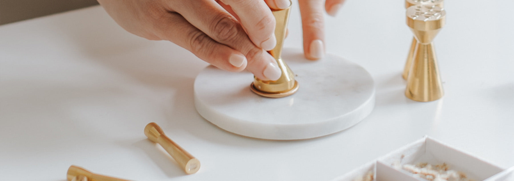 Hand pressing a brass wax seal stamp onto hot sealing wax on a white marble base with premium wax seal tools for wedding invitations and stationery.