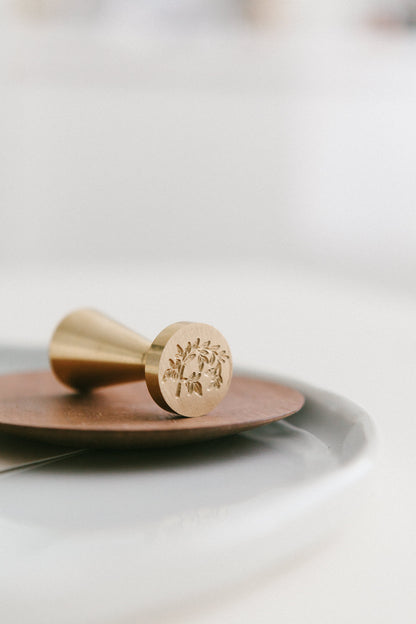 A brass wax seal stamp with Jasmine Vine design styled on a wooden and white ceramic plate