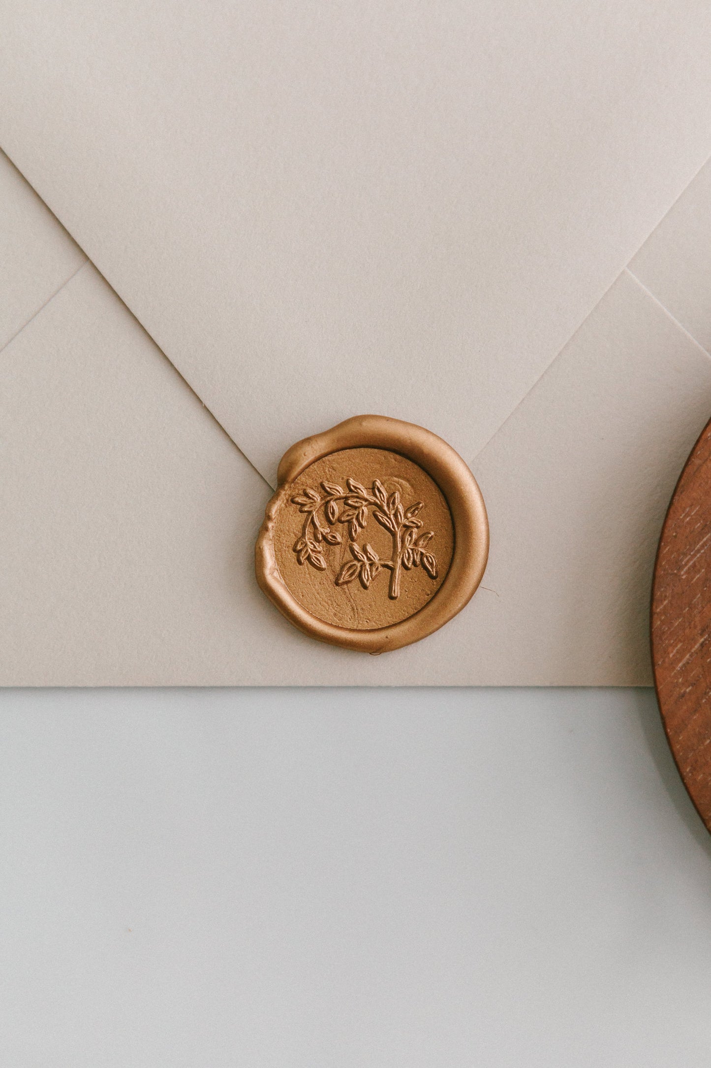 A close-up of a golden Jasmine Vine wax seal, styled on a beige sealed envelope on a white surface