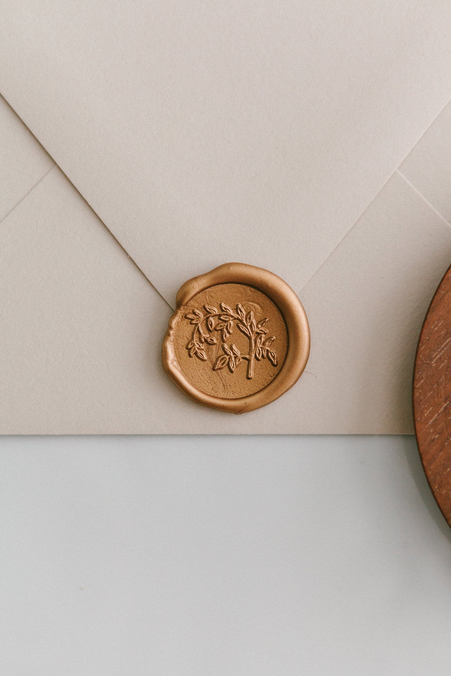 A close-up of a golden Jasmine Vine wax seal, styled on a beige sealed envelope on a white surface