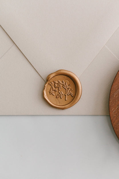 A close-up of a golden Jasmine Vine wax seal, styled on a beige sealed envelope on a white surface