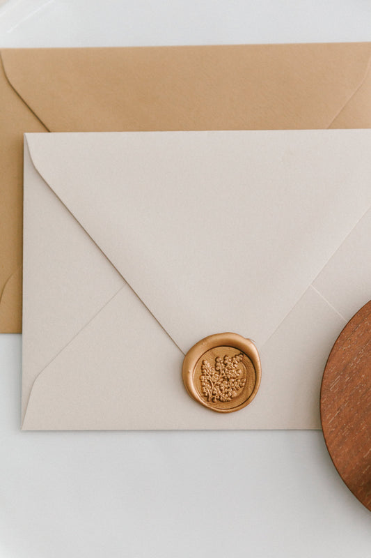 A golden maidenhair fern wax seal, styled on a beige sealed envelope and a wooden dish on the side