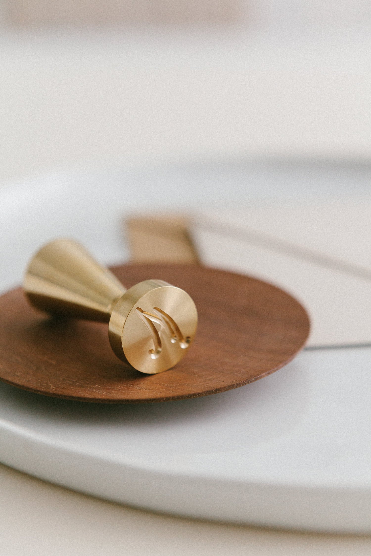 A brass wax seal stamp with M monogram design styled on a wooden and white ceramic plate