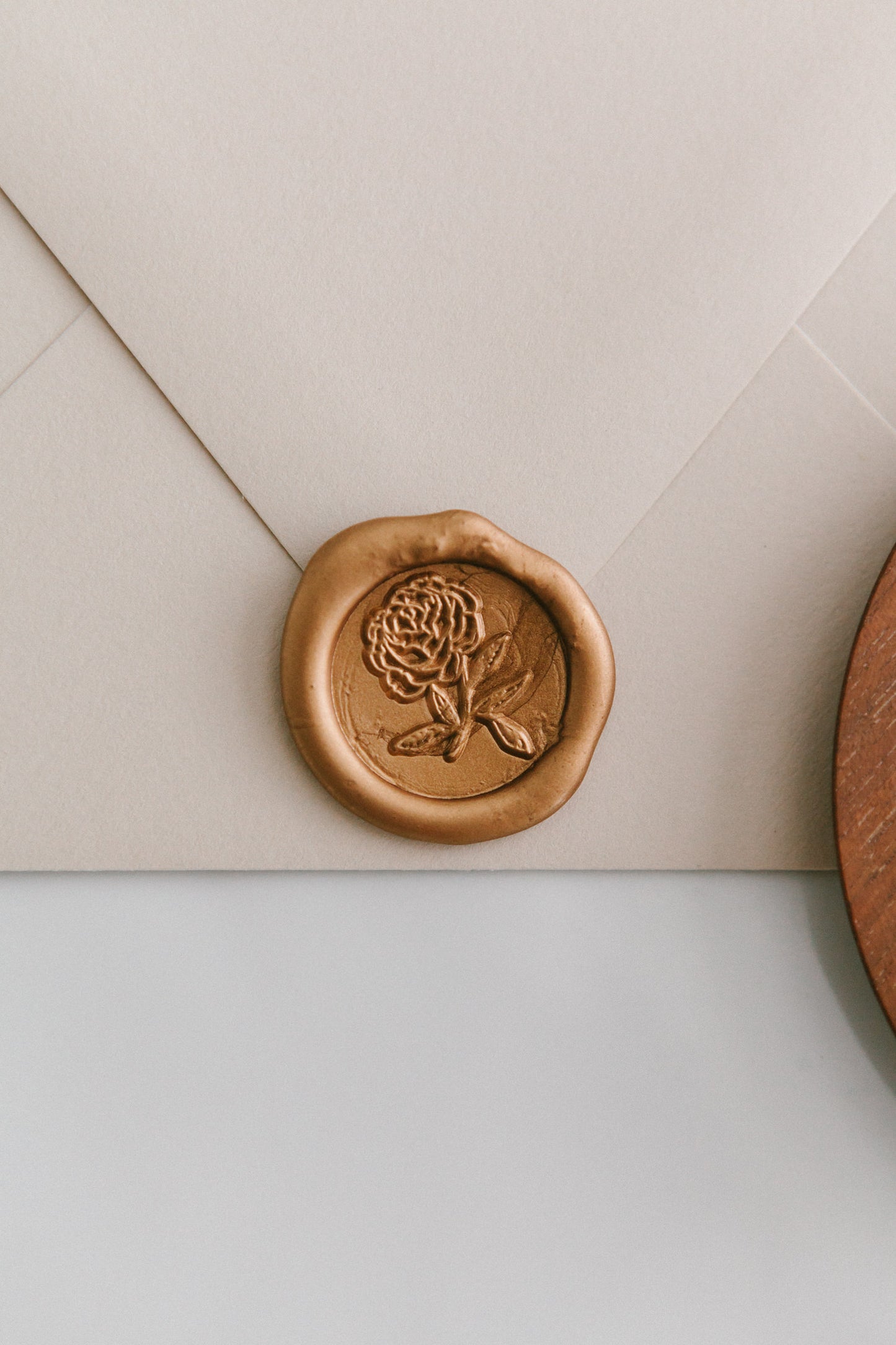 A close-up of a golden heirloom peony wax seal, styled on a beige sealed envelope on a white surface