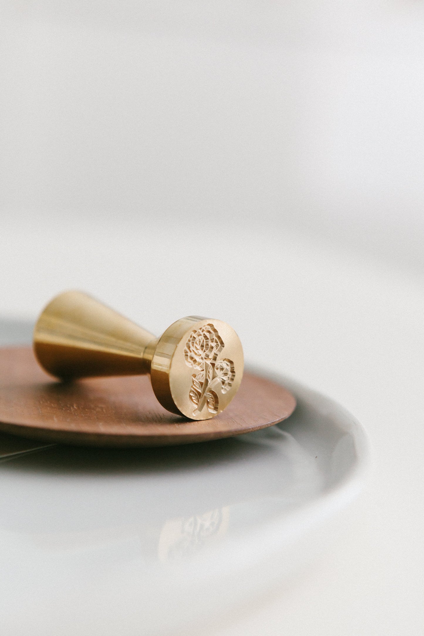 A brass wax seal stamp with heirloom peony design styled on a wooden and white ceramic plate
