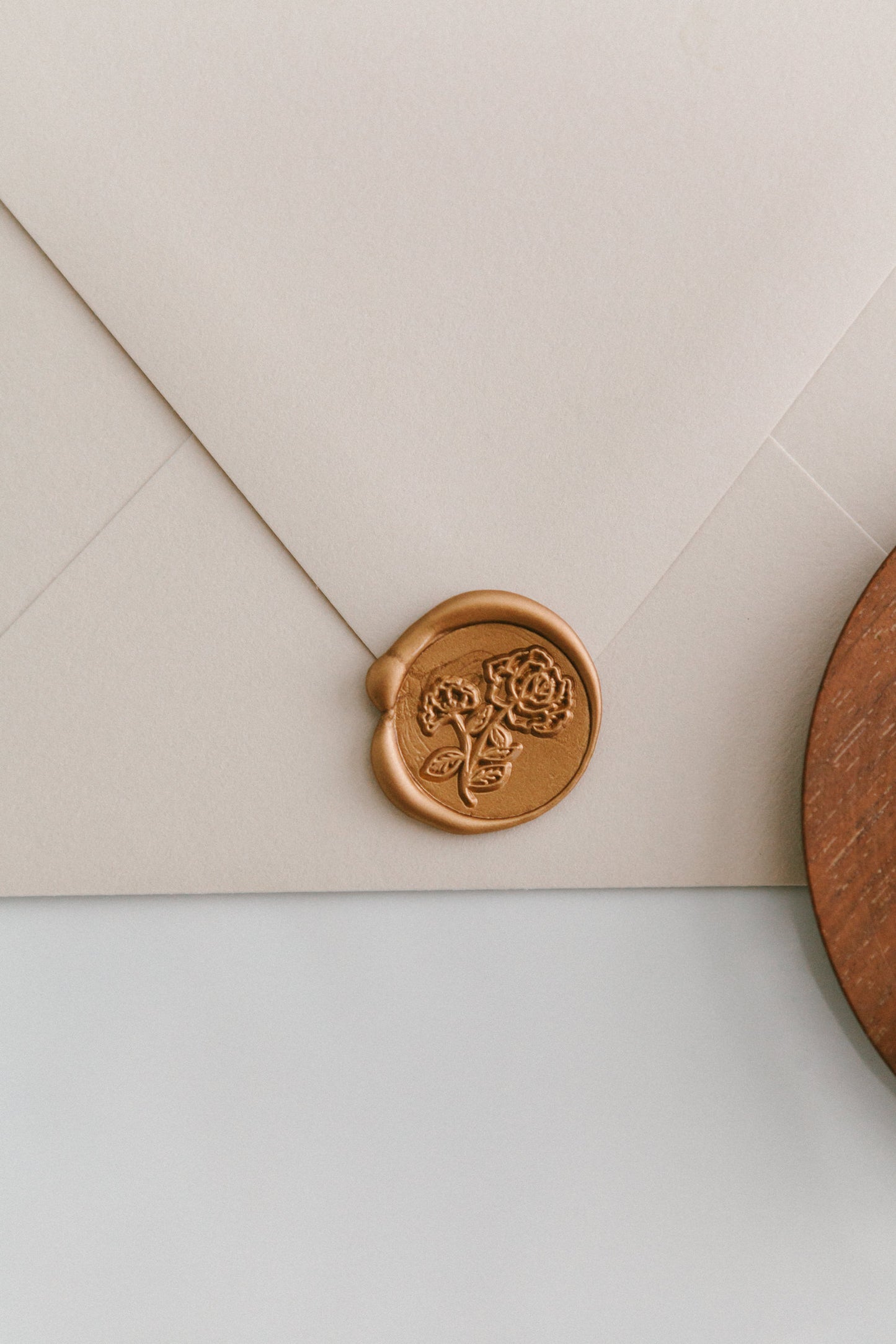A golden heirloom peony wax seal, styled on a beige sealed envelope and a wooden dish on the side