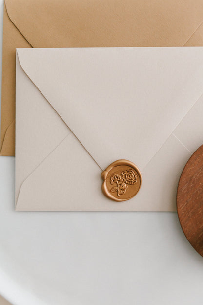A golden heirloom peony wax seal, styled on a beige sealed envelope and a wooden dish on the side