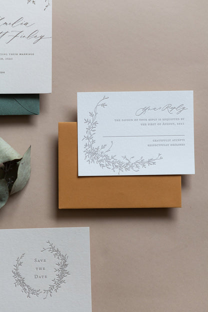 RSVP card with botanical vine illustration and embossed text on white cardstock with mustard envelope