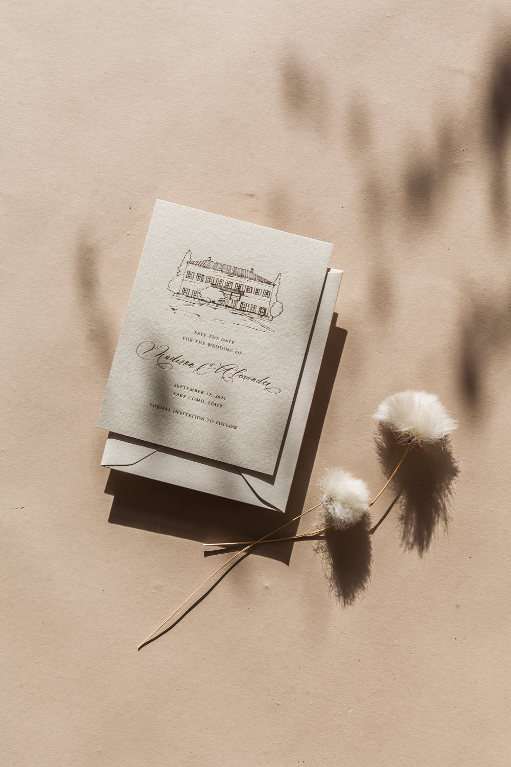 Neutral wedding save the date with custom venue sketch, calligraphy names, and envelope flat lay with soft dried florals