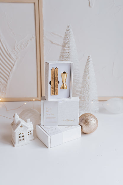 Elegant brass wax seal set with two gold wax sticks in luxury packaging, styled with holiday decor in a winter-themed setting