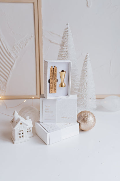 Elegant brass wax seal set with two gold wax sticks in luxury packaging, styled with holiday decor in a winter-themed setting