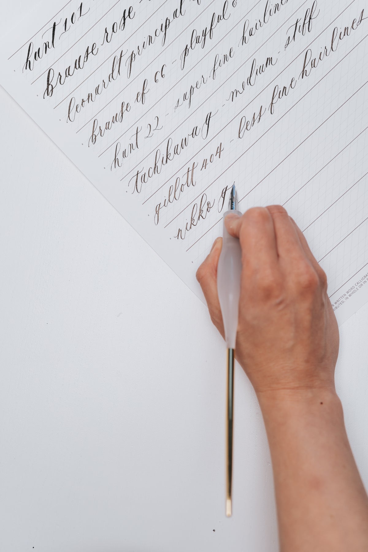 Hand holding a white quartz resin straight pen with a gold tail, writing on a calligraphy practice sheet