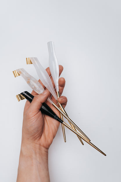 A hand holding four calligraphy pens with gold metal tails in white, rose, and black colored quartz