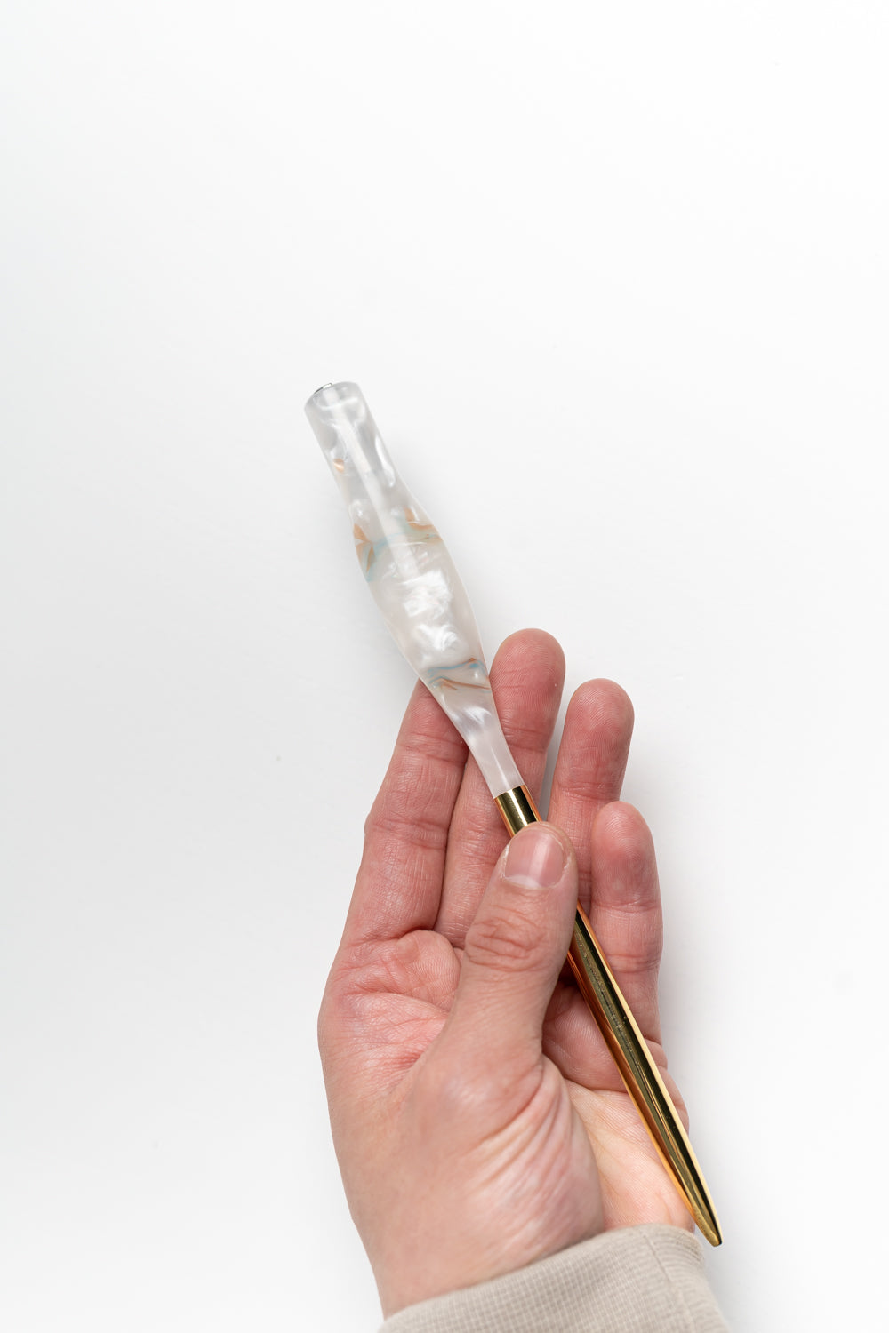 Hand holding a handmade calligraphy pen with a rose quartz resin body and gold tail