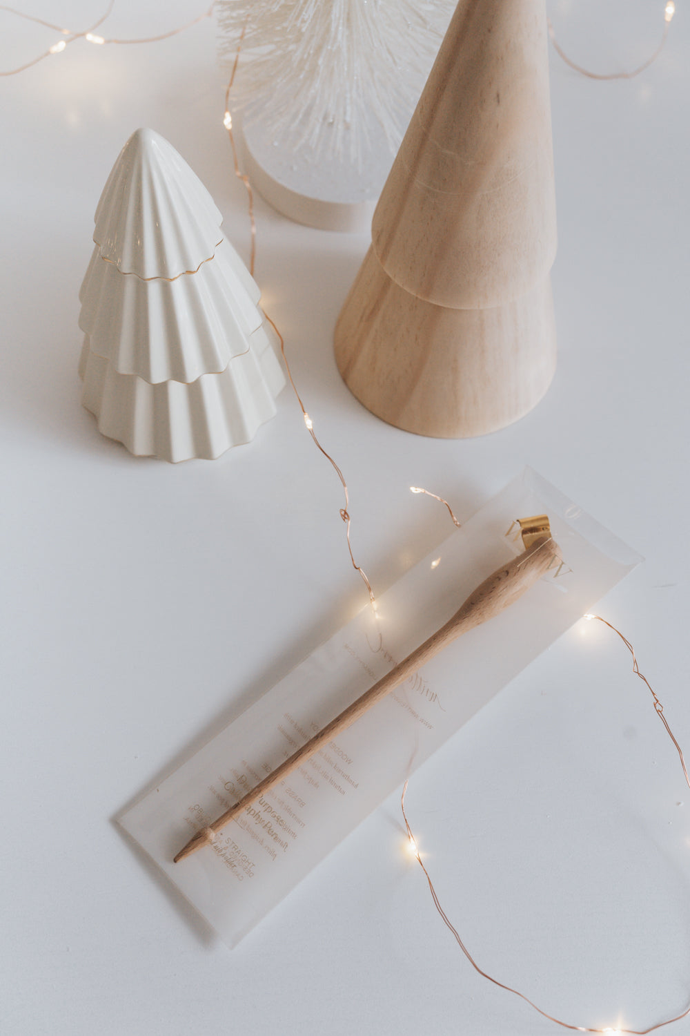 Wooden modern calligraphy pen in festive packaging with warm holiday decor, featuring fairy lights and ceramic tree decorations