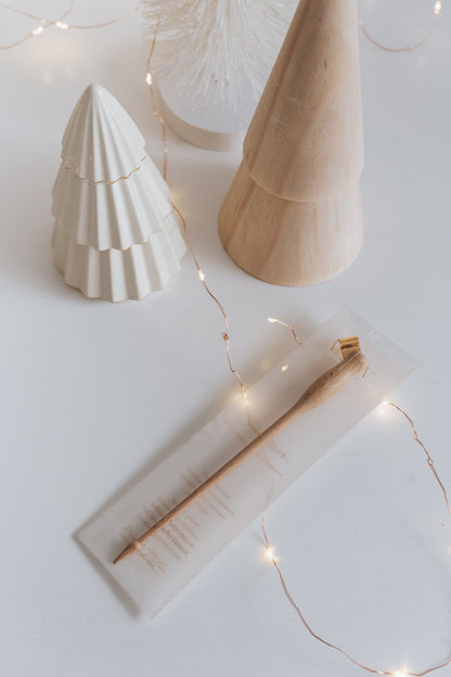 Wooden modern calligraphy pen in festive packaging with warm holiday decor, featuring fairy lights and ceramic tree decorations