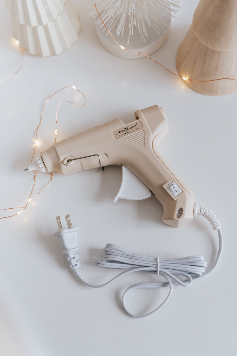 A beige Dual-Heat Glue Gun on a white surface surrounded with fairy lights and festive decor