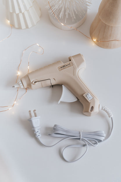 A beige Dual-Heat Glue Gun on a white surface surrounded with fairy lights and festive decor