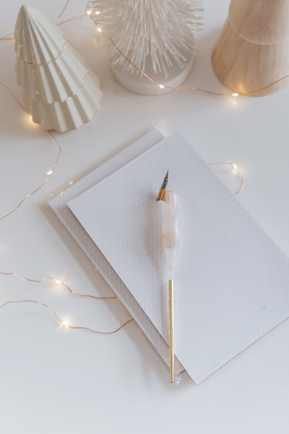 Resin calligraphy pen on slanted grid notepad surrounded by decorative trees and fairy lights