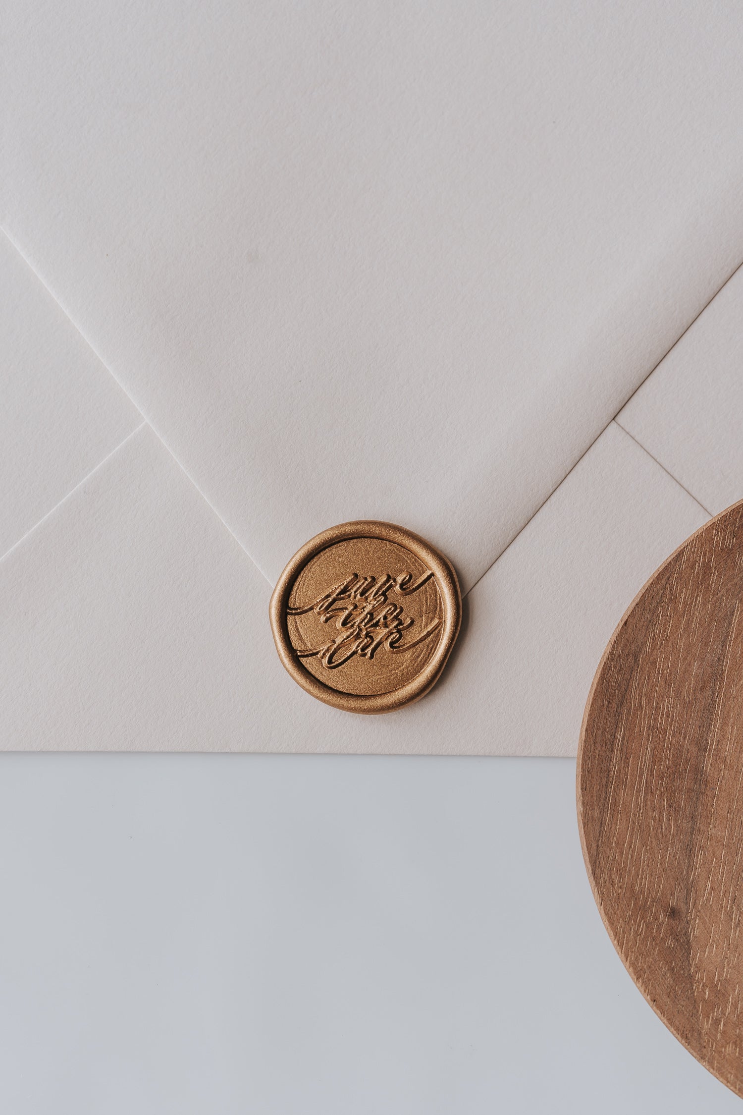 A beige envelope featuring a golden wax seal with Save the Date spelled out in modern calligraphy for wedding invitations