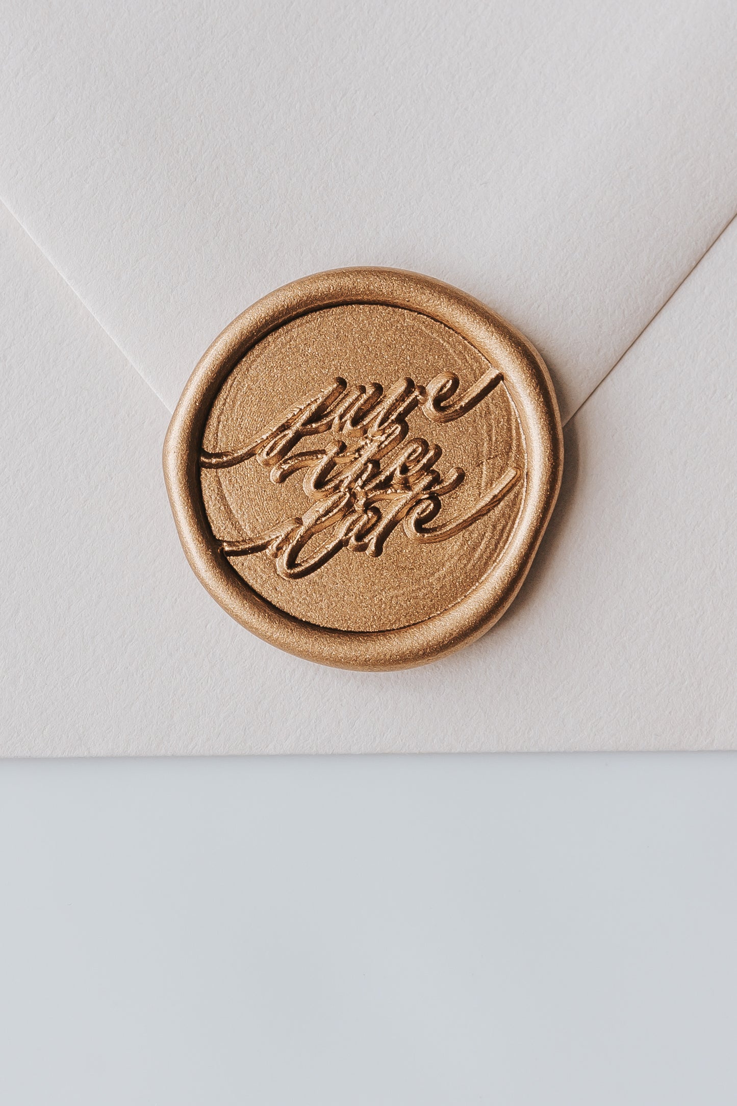 A beige envelope featuring a golden wax seal with Save the Date spelled out in modern calligraphy for wedding invitations