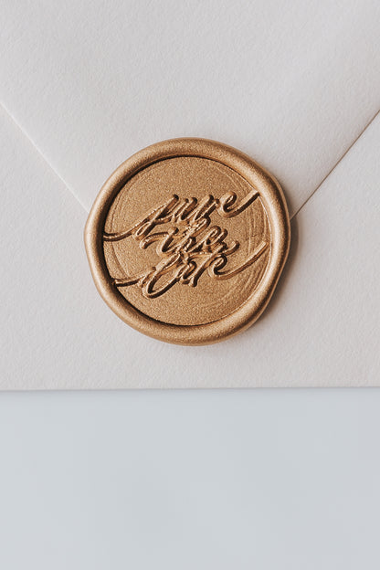 A beige envelope featuring a golden wax seal with Save the Date spelled out in modern calligraphy for wedding invitations