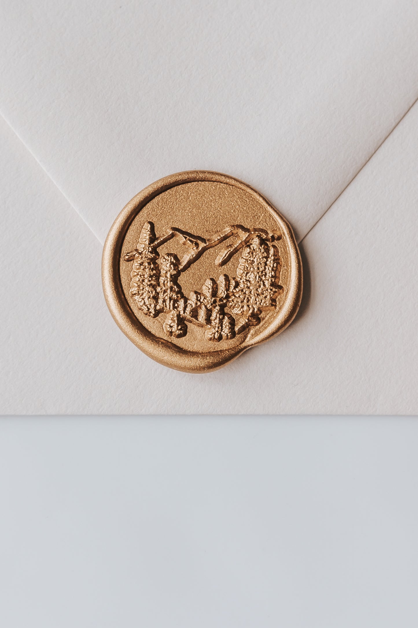 A close-up of a golden trees wax seal, styled on a beige sealed envelope on a white surface
