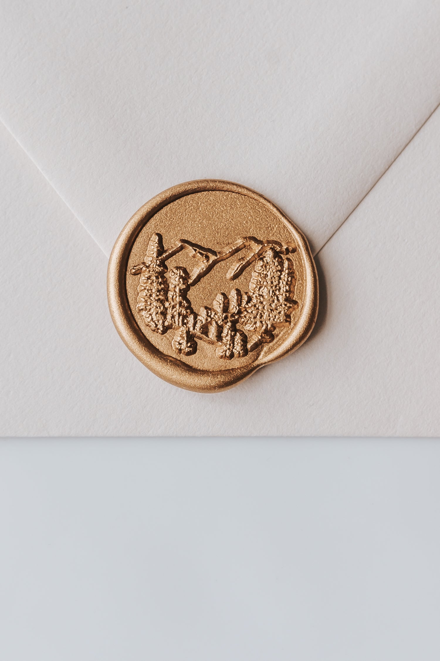 A close-up of a golden trees wax seal, styled on a beige sealed envelope on a white surface