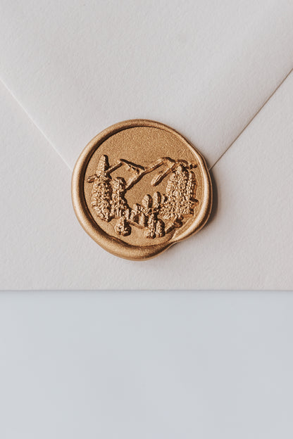 A close-up of a golden trees wax seal, styled on a beige sealed envelope on a white surface