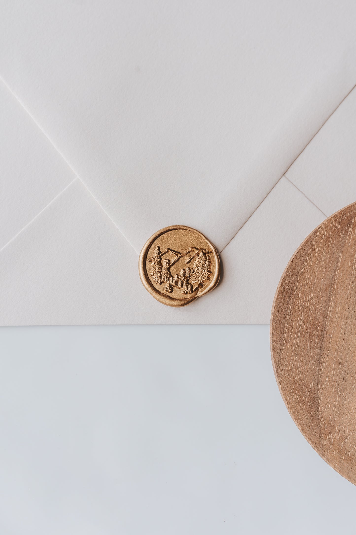 A golden trees wax seal, styled on a beige sealed envelope and a wooden dish on the side