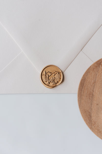 A golden trees wax seal, styled on a beige sealed envelope and a wooden dish on the side