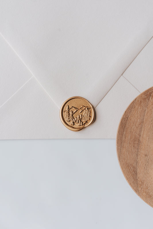 A golden trees wax seal, styled on a beige sealed envelope and a wooden dish on the side