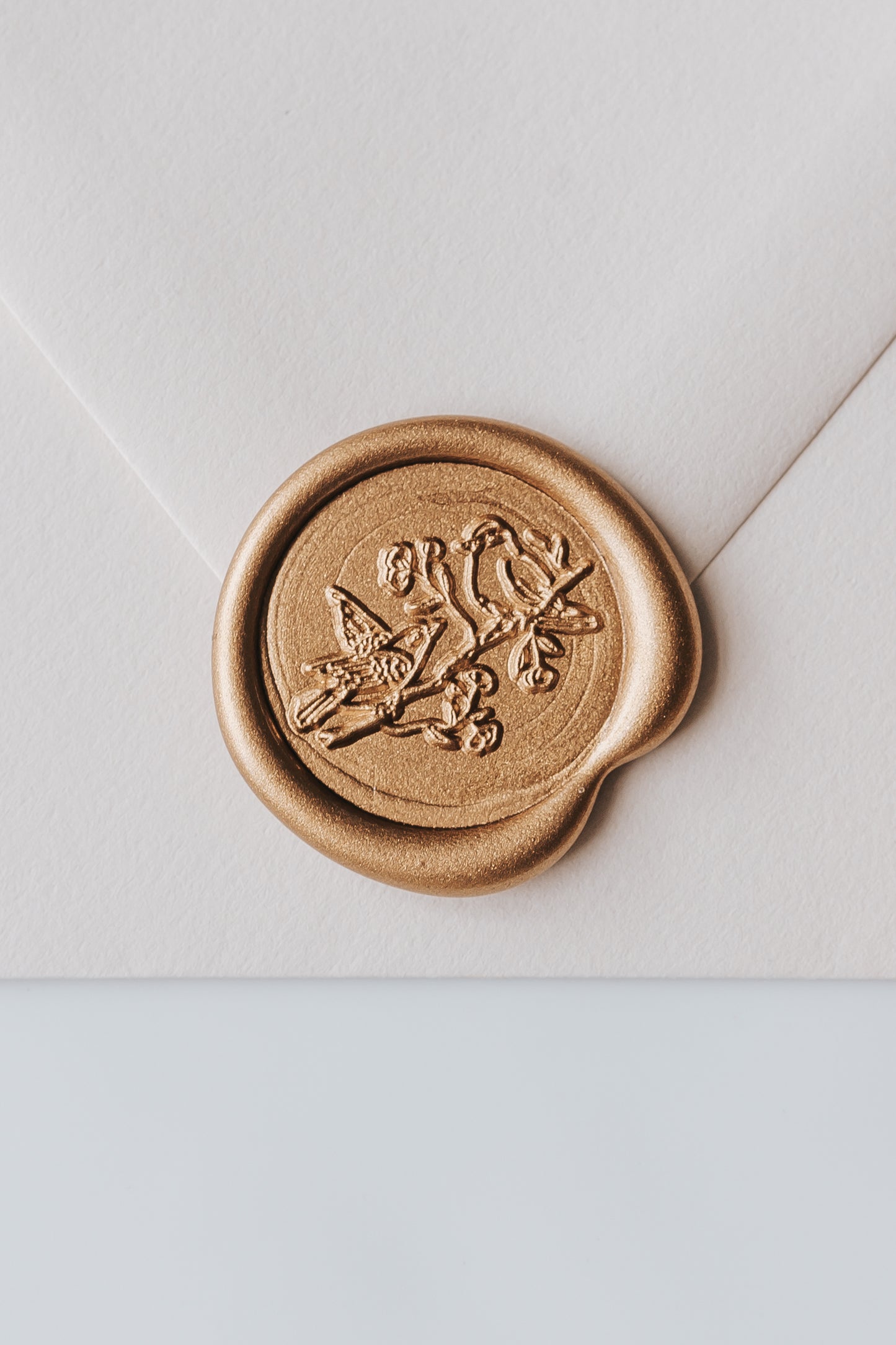 A close-up of a golden birds wax seal, styled on a beige sealed envelope on a white surface