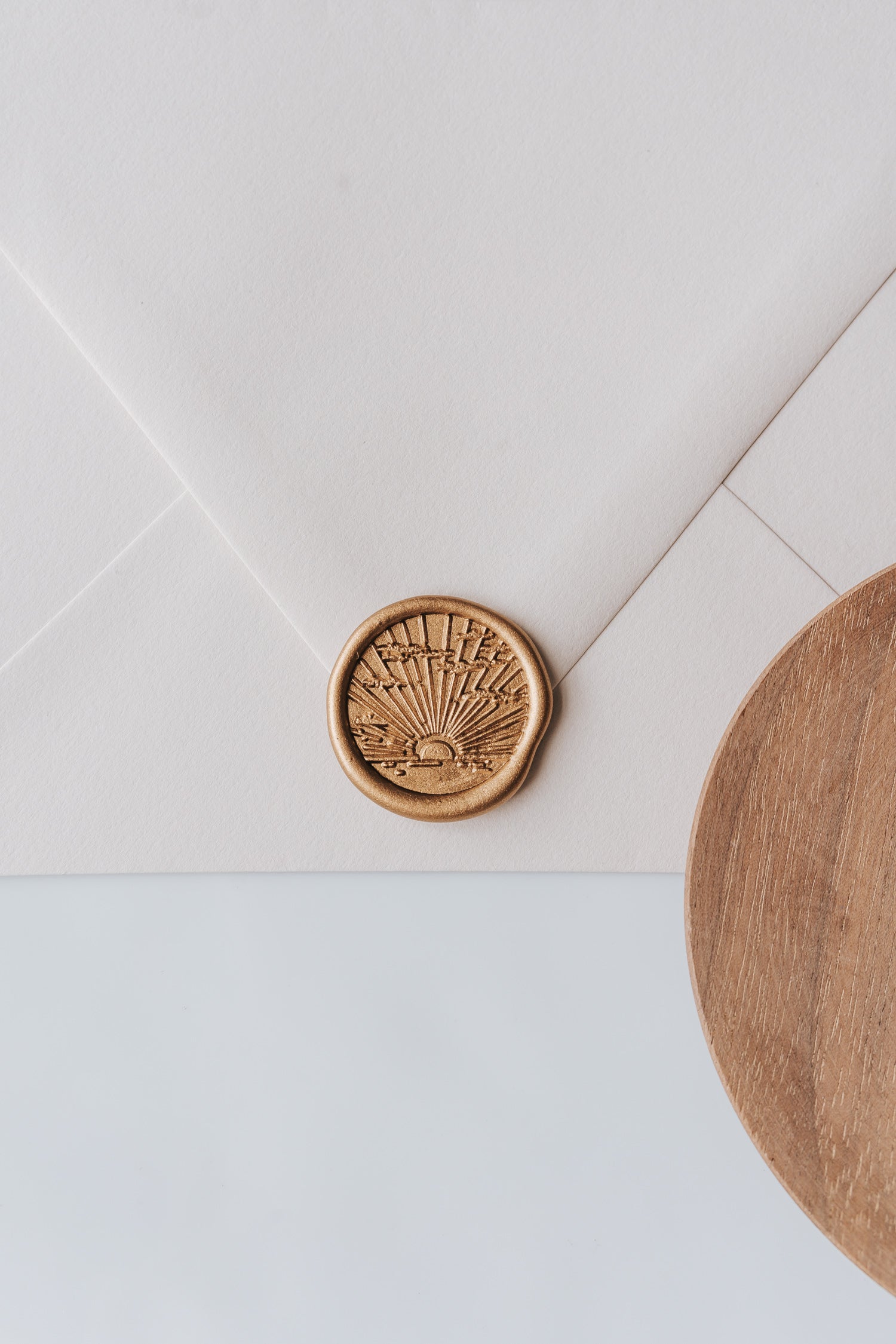 A golden sunrise wax seal, styled on a beige sealed envelope and a wooden dish on the side