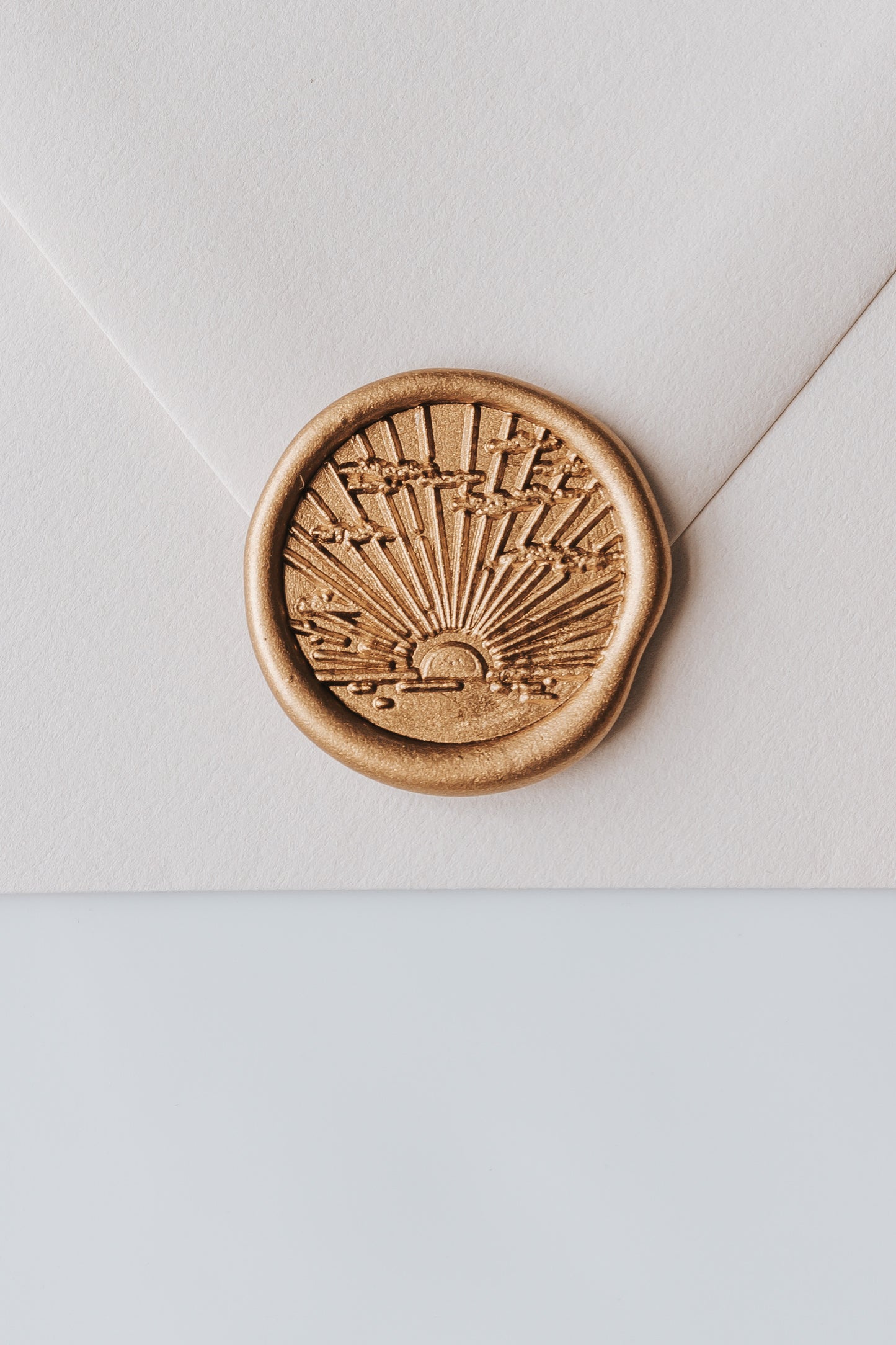 A close-up of a golden sunrise wax seal, styled on a beige sealed envelope on a white surface