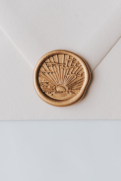 A close-up of a golden sunrise wax seal, styled on a beige sealed envelope on a white surface