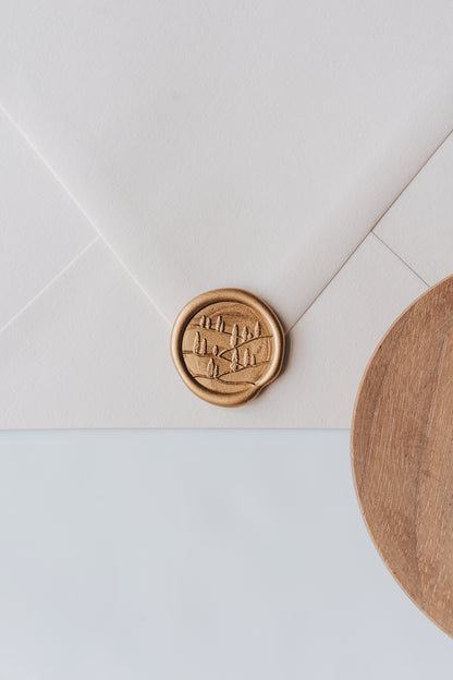 A golden Tuscany wax seal, styled on a beige sealed envelope and a wooden dish on the side