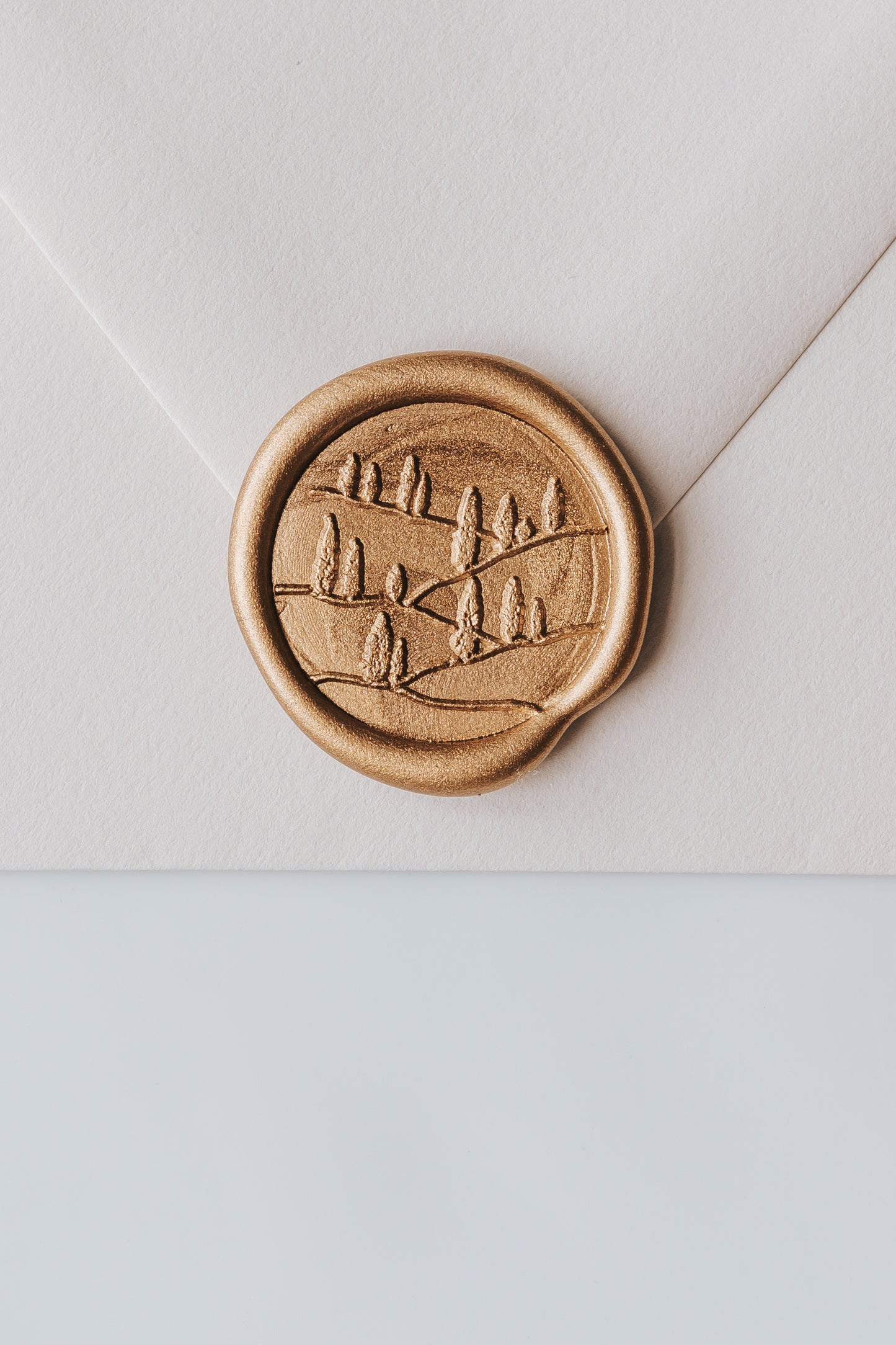A close-up of a golden Tuscany wax seal, styled on a beige sealed envelope on a white surface