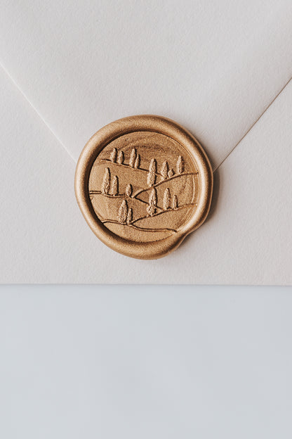 A close-up of a golden Tuscany wax seal, styled on a beige sealed envelope on a white surface
