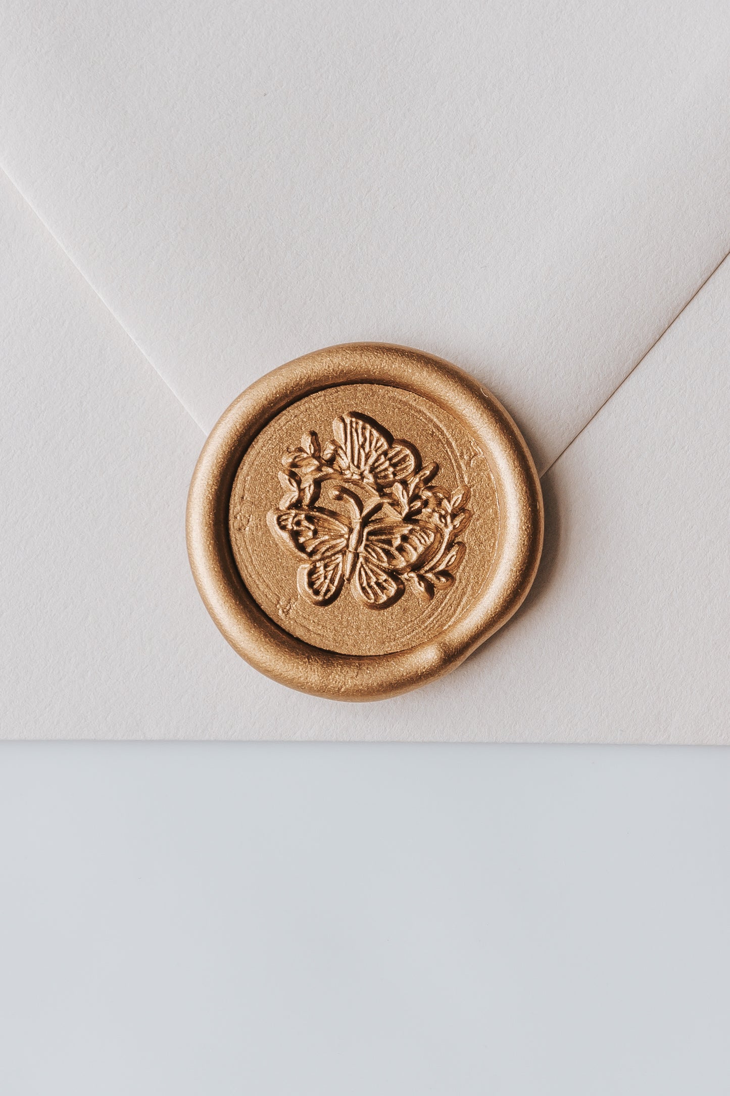A close-up of a golden butterflies wax seal, styled on a beige sealed envelope on a white surface