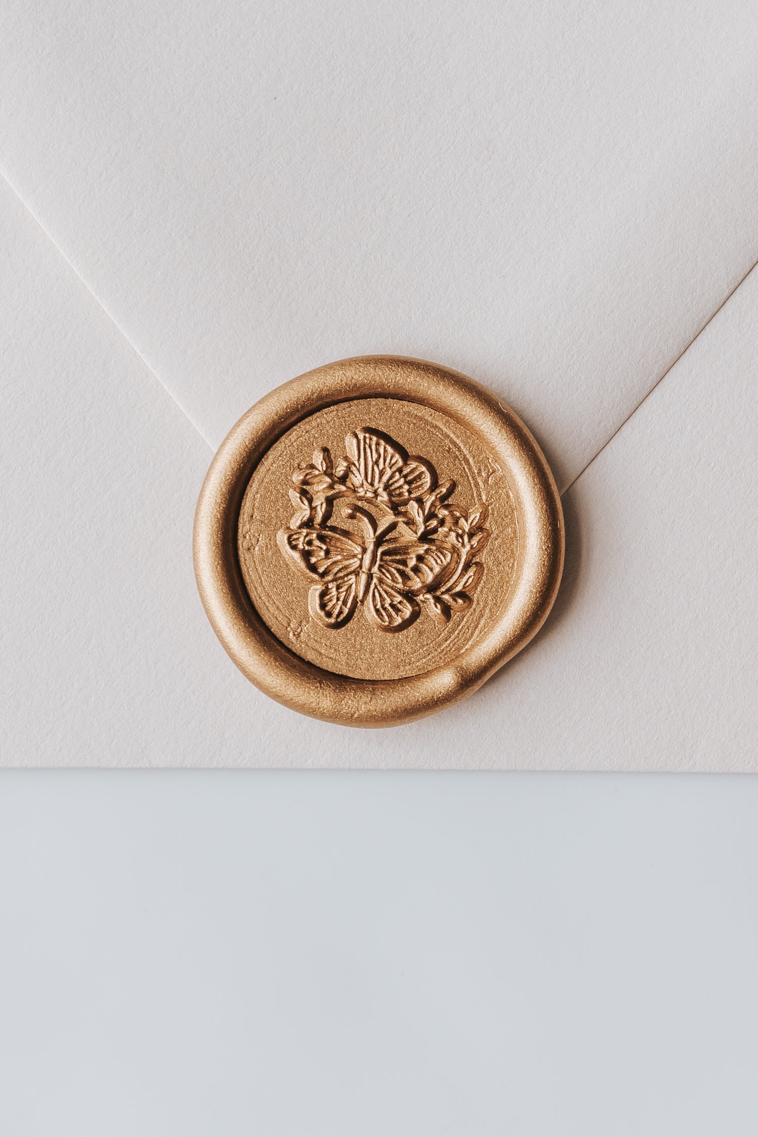 A close-up of a golden butterflies wax seal, styled on a beige sealed envelope on a white surface