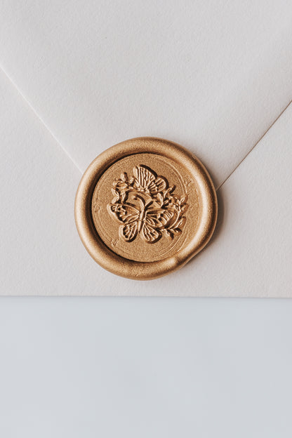 A close-up of a golden butterflies wax seal, styled on a beige sealed envelope on a white surface