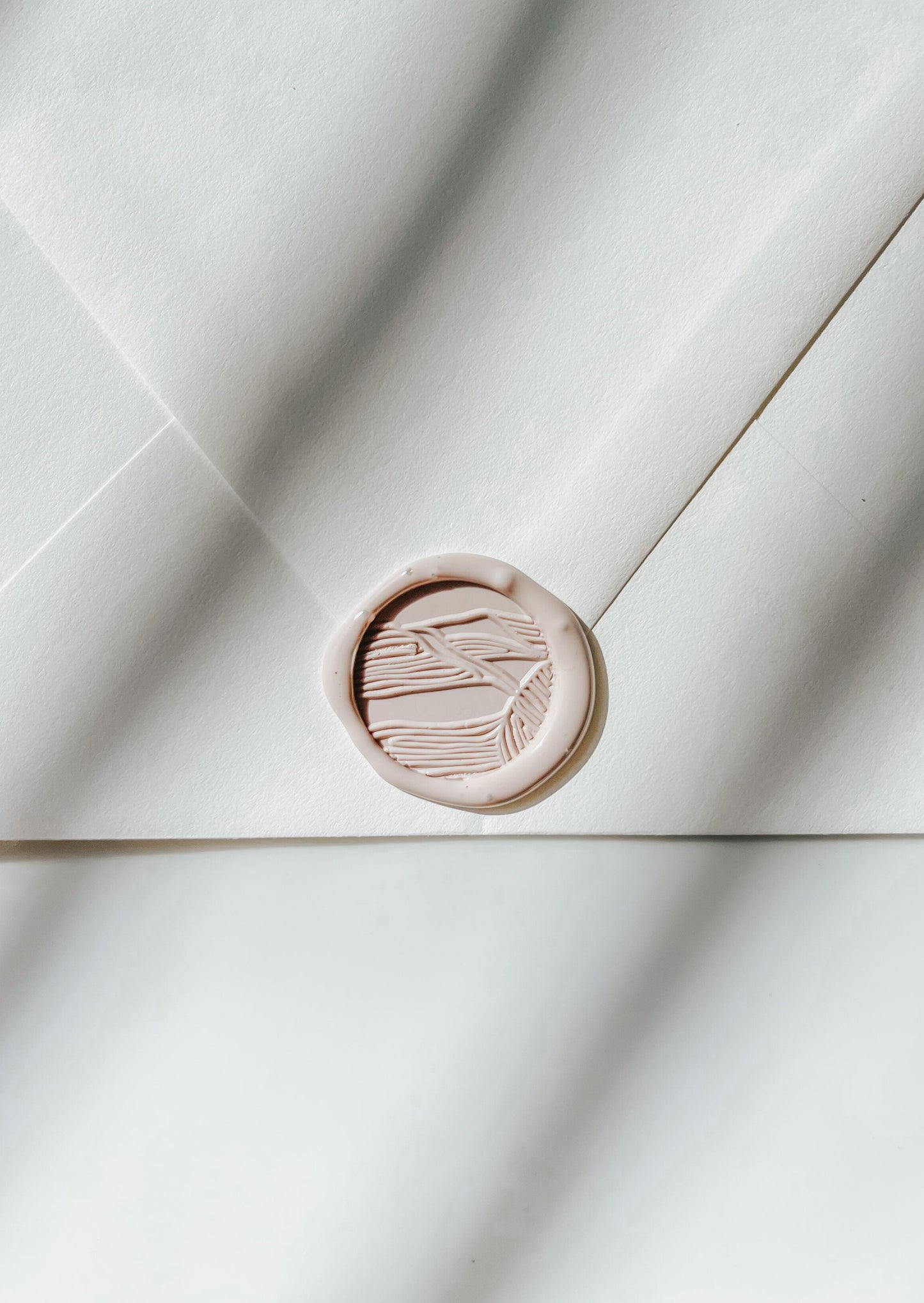 A close-up of a beige sand dunes wax seal, styled on a sealed envelope on a white surface