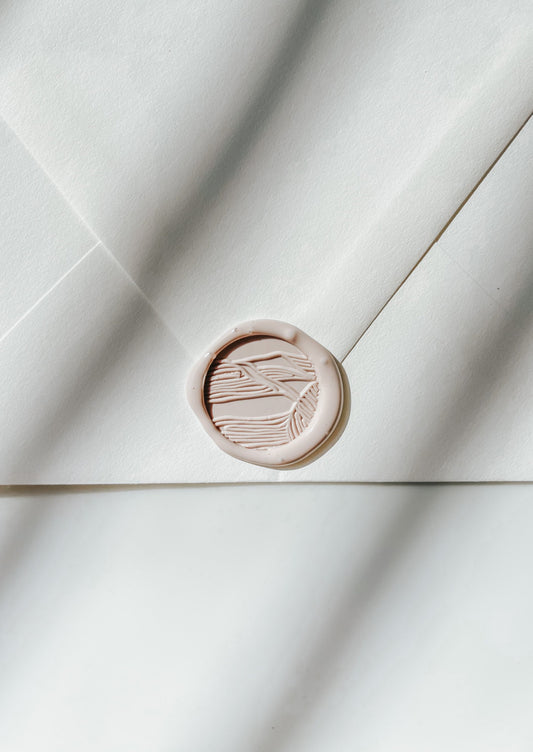 A close-up of a beige sand dunes wax seal, styled on a sealed envelope on a white surface