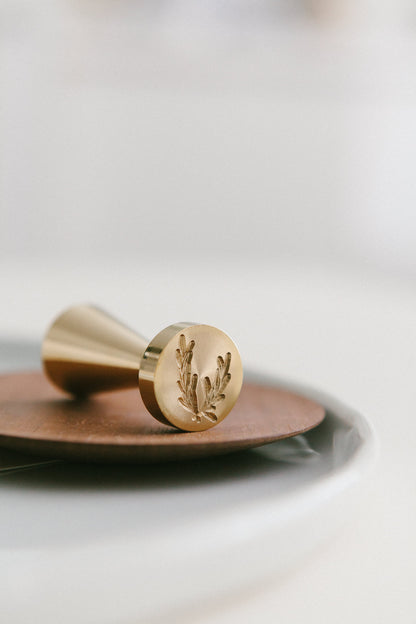 A close-up of a brass olive crest wax seal stamp on a wooden plate