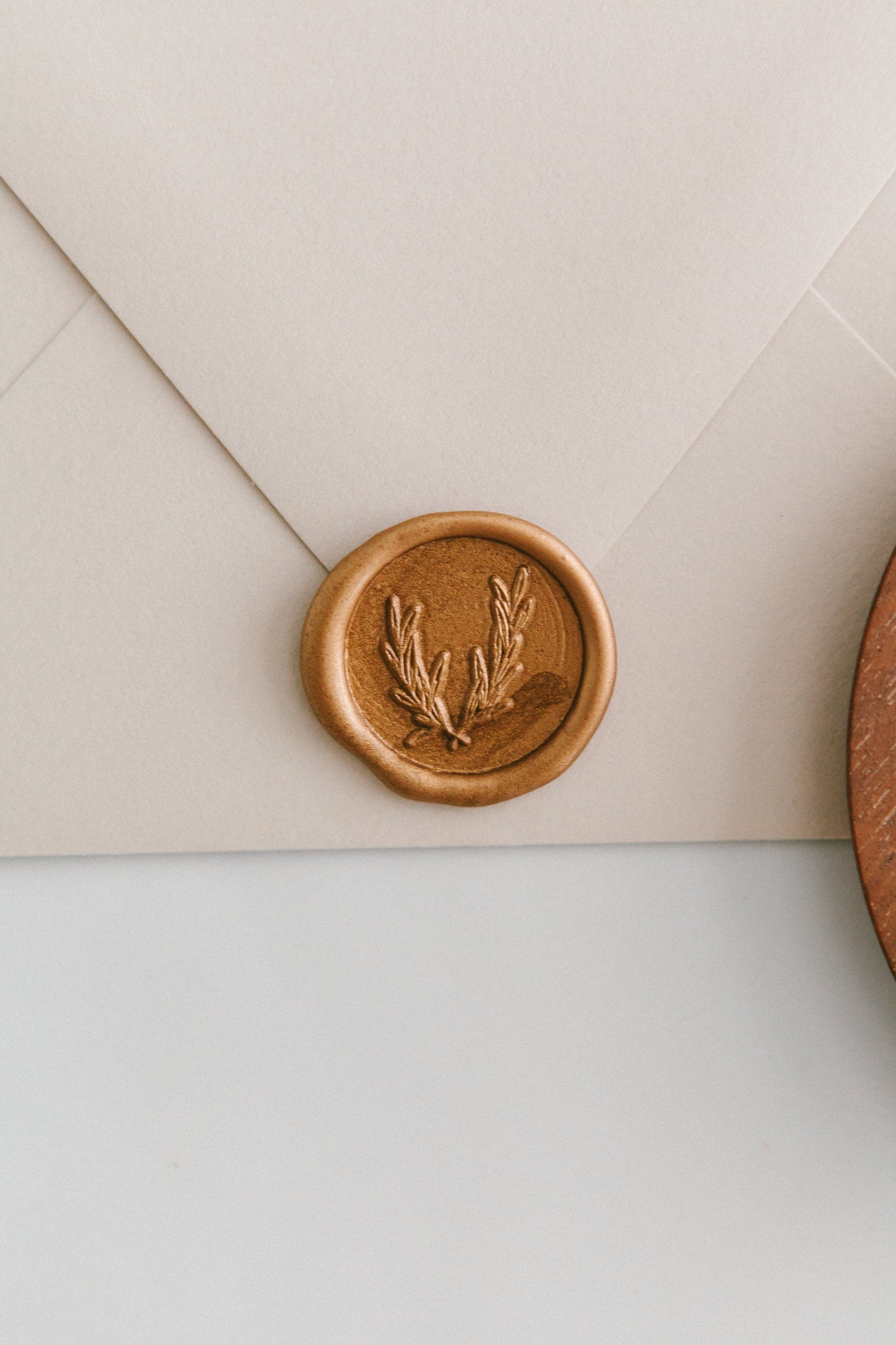 A close-up of a golden olive crest wax seal, styled on a beige sealed envelope on a white surface